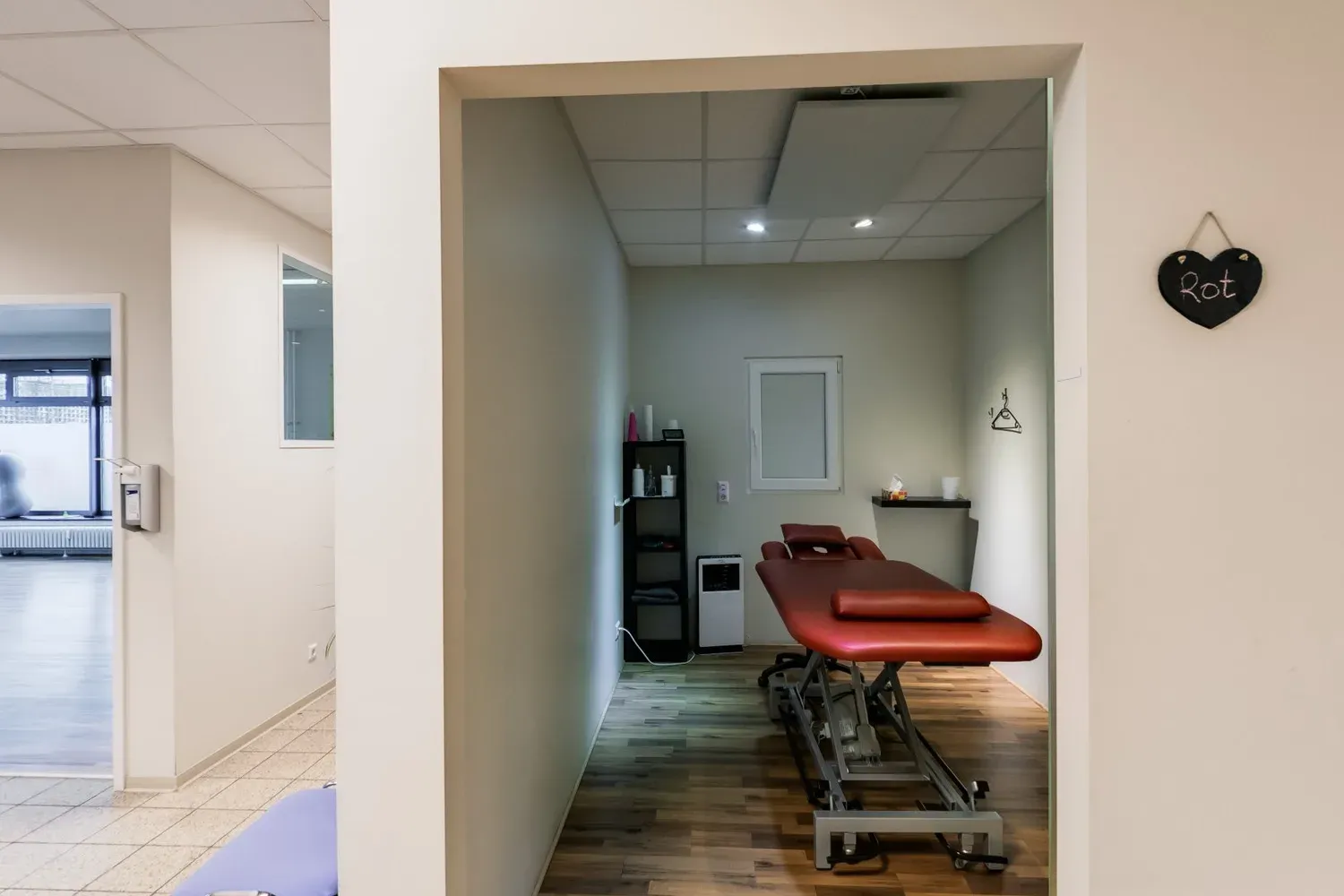 Blick in den Behandlungsraum Rot mit roter Therapieliege und Holzboden
