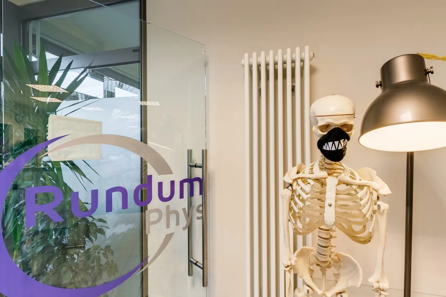 Eingangsbereich mit Anatomieskelett und der Glastür mit dem Logo von Rundum Gesund